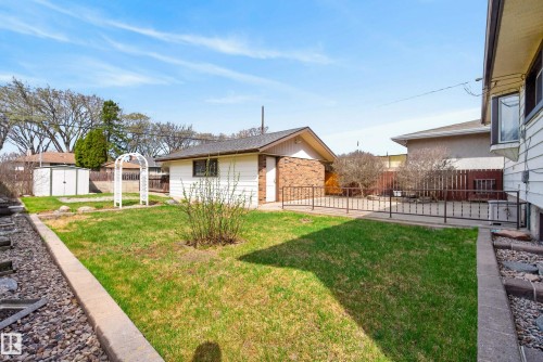 Expansive backyard featuring a manicured lawn, a detached accessory building with brick accents, and a white garden arbor - 12016 51 Street, Edmonton, AB - Outdoor