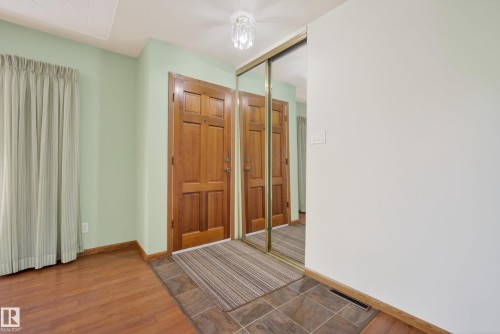 Entryway featuring two paneled wood doors, mirrored sliding closet doors, and mixed flooring with large format tiles and wood-finish planks - 12016 51 Street, Edmonton, AB - Indoor Photo Showing Other Room