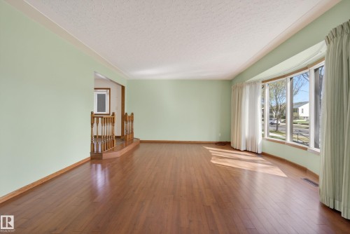 Spacious living area featuring wood-finish flooring, light green walls, and white crown molding - 12016 51 Street, Edmonton, AB - Indoor Photo Showing Other Room