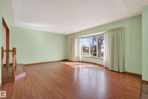 Spacious interior room featuring wood-finish flooring, light green wall paint, and a textured ceiling - 12016 51 Street, Edmonton, AB - Indoor Photo Showing Other Room