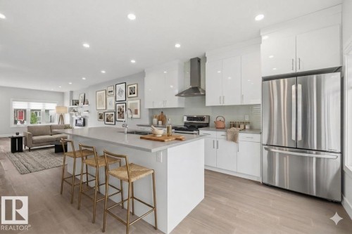 Modern kitchen featuring white glossy cabinetry, stainless steel appliances, a light-toned countertop island, a tile backsplash, and light wood-finish flooring - 9933 79 Street, Edmonton, AB - Indoor Photo Showing Kitchen With Stainless Steel Kitchen With Upgraded Kitchen
