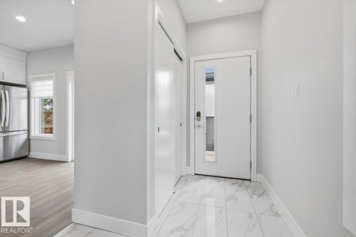 Entryway featuring large format white tile flooring, a solid panel front door with a vertical frosted glass insert, and a double-door closet - 9933 79 Street, Edmonton, AB - Indoor Photo Showing Other Room