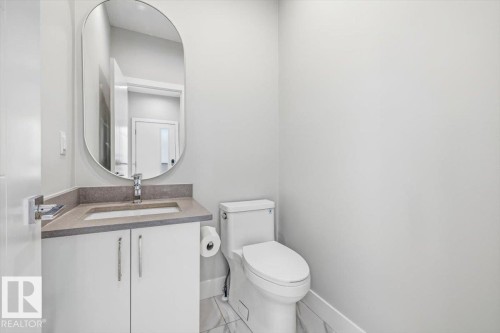 Powder room featuring a white vanity with integrated sink, stone-finish countertop, and a contemporary oval mirror - 9933 79 Street, Edmonton, AB - Indoor Photo Showing Bathroom