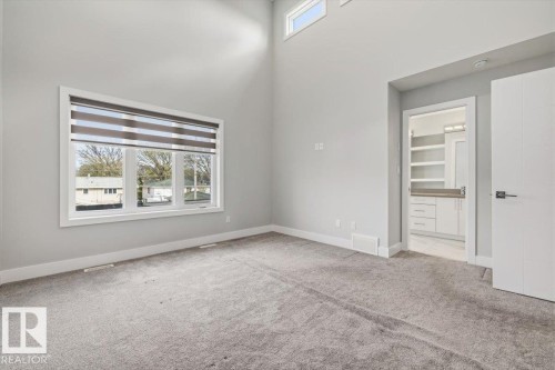 Spacious room featuring vaulted ceilings, a large window with blind treatments, light gray carpeting, and a doorway revealing a bathroom with a white vanity and built-in shelving - 9933 79 Street, Edmonton, AB - Indoor Photo Showing Other Room
