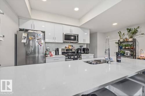 Modern kitchen featuring a large island with an undermount sink, stainless steel appliances, white flat-panel cabinetry, and a subway tile backsplash - 9933 79 Street, Edmonton, AB - Indoor Photo Showing Kitchen With Stainless Steel Kitchen With Double Sink