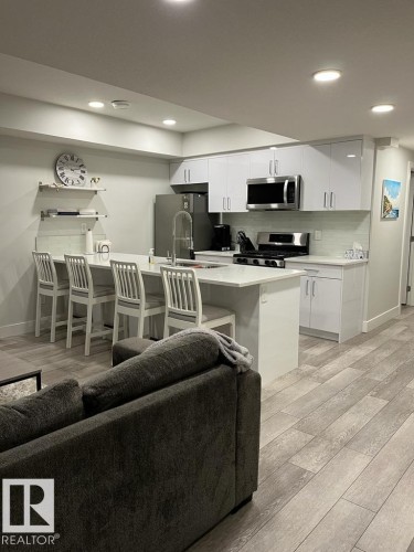 Modern kitchen featuring white cabinetry, stainless steel appliances, a white tile backsplash, and a large island with seating - 9933 79 Street, Edmonton, AB - Indoor Photo Showing Kitchen With Stainless Steel Kitchen