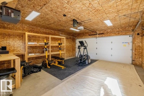 Garage space featuring a white sectional garage door, exposed OSB walls and ceiling, and a concrete floor - 9933 79 Street, Edmonton, AB - Indoor Photo Showing Garage