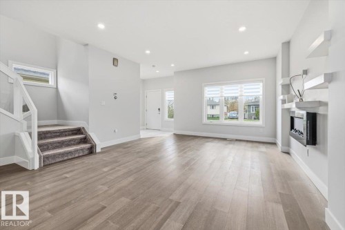 Open-concept living area with wood-finish flooring, recessed lighting, and a contemporary wall-mounted fireplace - 9933 79 Street, Edmonton, AB - Indoor Photo Showing Other Room With Fireplace