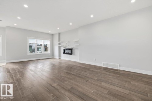Spacious room featuring wood-finish flooring, recessed lighting, a modern wall-mounted fireplace, and multiple windows with blinds - 9933 79 Street, Edmonton, AB - Indoor Photo Showing Living Room With Fireplace