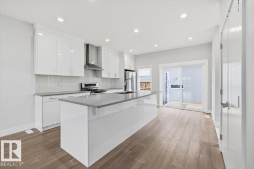 Contemporary kitchen featuring a large island, white cabinetry, integrated stainless steel appliances, wood-finish flooring, and sliding glass door access to an outdoor area - 9933 79 Street, Edmonton, AB - Indoor Photo Showing Kitchen With Upgraded Kitchen