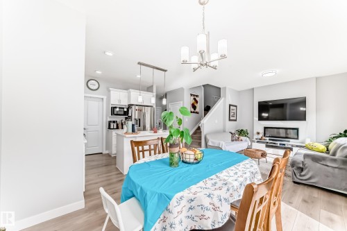 Open concept living area featuring light-colored flooring, a kitchen with white cabinetry and stainless steel appliances, and a living room with a modern fireplace - 19635 29 Avenue, Edmonton, AB - Indoor