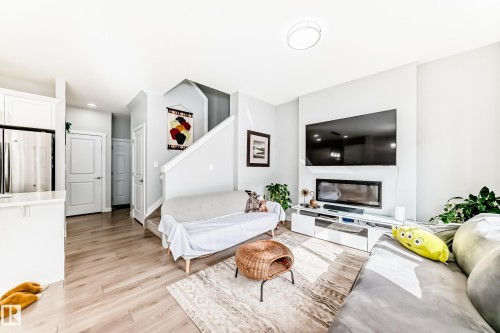 The open-concept living area features light-colored flooring, a modern fireplace, and a staircase - 19635 29 Avenue, Edmonton, AB - Indoor Photo Showing Living Room With Fireplace
