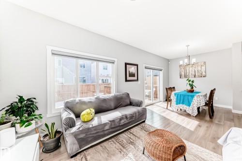 This open-concept living area features light wood flooring, a large window providing natural light, and a sliding glass door leading to the outdoors - 19635 29 Avenue, Edmonton, AB - Indoor