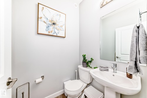 Bathroom featuring a pedestal sink, a toilet, a wall-mounted mirror, and wood flooring - 19635 29 Avenue, Edmonton, AB - Indoor Photo Showing Bathroom
