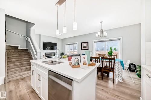 Bright open concept living area featuring a kitchen island with a sink and pendant lighting, hardwood flooring, and a sliding glass door - 19635 29 Avenue, Edmonton, AB - Indoor