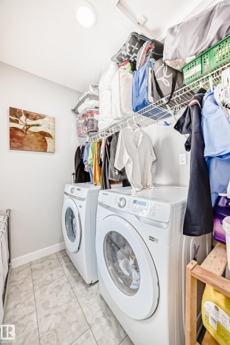 The property features a dedicated laundry area with two front-loading machines, overhead wire shelving for storage, and light-colored tile flooring - 19635 29 Avenue, Edmonton, AB - Indoor Photo Showing Laundry Room