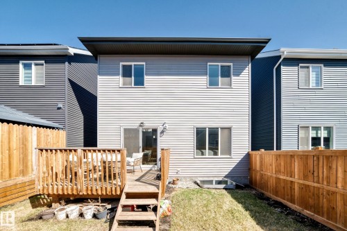Rear facade featuring light-colored horizontal siding, a private wood deck with steps to the lawn, a sliding glass door, and multiple windows - 19635 29 Avenue, Edmonton, AB - Outdoor With Exterior