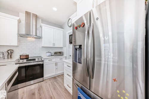 The kitchen features white cabinetry, stainless steel appliances, a white subway tile backsplash, and light wood flooring - 19635 29 Avenue, Edmonton, AB - Indoor Photo Showing Kitchen With Upgraded Kitchen