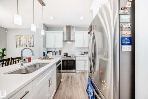 The kitchen features white cabinetry, stainless steel appliances, a white subway tile backsplash, and light-colored wood flooring - 19635 29 Avenue, Edmonton, AB - Indoor Photo Showing Kitchen With Double Sink With Upgraded Kitchen