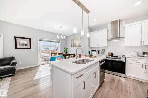 Modern kitchen featuring a white island with a double sink, stainless steel appliances, white cabinetry, and light wood flooring - 19635 29 Avenue, Edmonton, AB - Indoor Photo Showing Kitchen With Double Sink