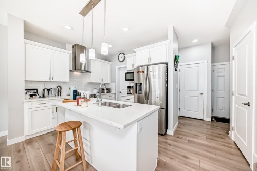 Contemporary kitchen featuring white cabinetry, a kitchen island with a sink, stainless steel appliances, and light wood flooring - 19635 29 Avenue, Edmonton, AB - Indoor Photo Showing Kitchen With Double Sink With Upgraded Kitchen