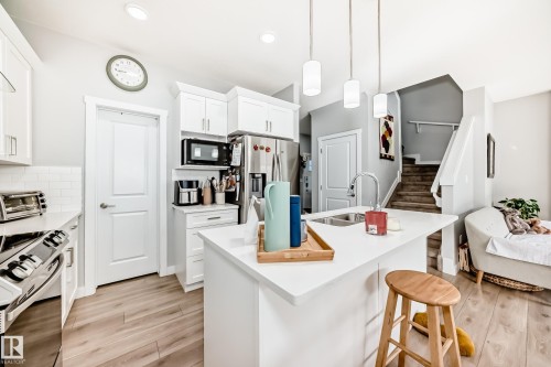The kitchen features white cabinetry, a kitchen island with a sink and pendant lighting, and stainless steel appliances including a refrigerator and microwave - 19635 29 Avenue, Edmonton, AB - Indoor Photo Showing Kitchen With Double Sink
