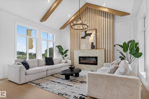 Vaulted ceiling living space with exposed wood beams, a contemporary fireplace with a stone surround, and an accent wall featuring vertical wood paneling - 711 166 Avenue, Edmonton, AB - Indoor Photo Showing Living Room With Fireplace