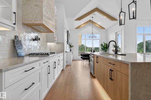 Spacious kitchen featuring an extended island with a built-in sink and a black gooseneck faucet, white shaker-style cabinetry, and light wood-finish flooring - 711 166 Avenue, Edmonton, AB - Indoor Photo Showing Kitchen With Upgraded Kitchen