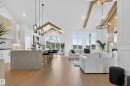 Open-concept living area featuring a vaulted ceiling with exposed beams, wood-finish flooring, a kitchen island with seating, a tile backsplash, and large windows - 711 166 Avenue, Edmonton, AB  - Indoor 