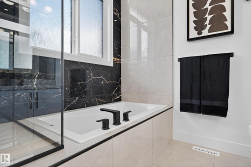 Built-in soaking tub featuring matte black fixtures, set against black marble-look wall tiling and light-toned tile flooring - 711 166 Avenue, Edmonton, AB - Indoor Photo Showing Bathroom