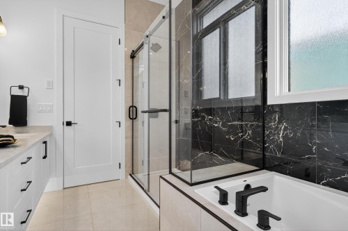 Spacious bathroom featuring a white soaking tub with matte black fixtures, a walk-in shower with clear glass enclosure and black marble-look tile, and light-toned floor tile - 711 166 Avenue, Edmonton, AB - Indoor Photo Showing Bathroom