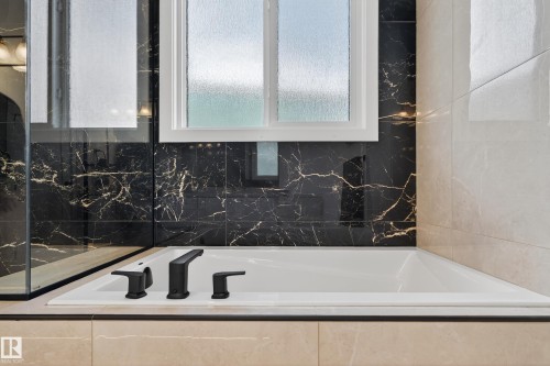 Built-in soaking tub with matte black fixtures, set against black and gold veined tile surround - 711 166 Avenue, Edmonton, AB - Indoor