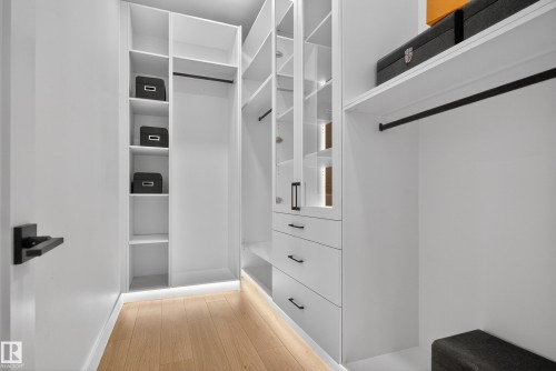 Custom white closet system featuring integrated shelving, multiple hanging rods, built-in drawers with matte black hardware, glass-front cabinetry, and wood-finish flooring - 711 166 Avenue, Edmonton, AB - Indoor