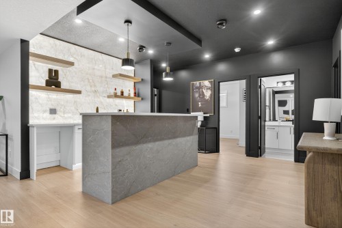 Modern entertainment space featuring light wood-finish flooring, a contemporary wet bar with a stone-finish countertop, and a backlit marble-look accent wall with floating shelves - 711 166 Avenue, Edmonton, AB - Indoor