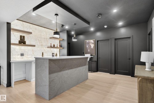 Custom bar area featuring a waterfall countertop, light wood-finish flooring, dark paneled doors, recessed lighting, and a decorative stone wall with floating shelves - 711 166 Avenue, Edmonton, AB - Indoor