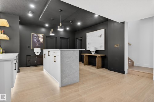 Contemporary kitchen island featuring a light-toned stone-finish countertop, light wood-finish flooring, recessed ceiling lighting, pendant light fixtures, and a staircase with wood treads - 711 166 Avenue, Edmonton, AB - Indoor Photo Showing Other Room