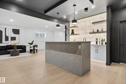 Modern entertainment space featuring wood-finish flooring, a contemporary wet bar with a stone-clad island, and an illuminated accent wall with floating shelves - 711 166 Avenue, Edmonton, AB - Indoor Photo Showing Other Room