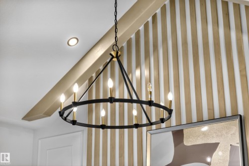 Black and gold-tone chandelier with candelabra bulbs, recessed ceiling lighting, and a decorative slatted wood-finish wall accent - 711 166 Avenue, Edmonton, AB - Indoor Photo Showing Other Room