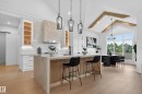 Modern kitchen featuring a large central island with slatted wood detailing, white cabinetry, a stone-clad range hood, and light wood-finish flooring - 711 166 Avenue, Edmonton, AB  - Indoor 
