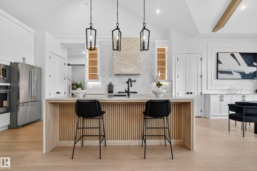 Contemporary kitchen featuring a light wood-finish island with vertical slat detailing, a light countertop, and three black pendant lights - 711 166 Avenue, Edmonton, AB - Indoor Photo Showing Kitchen With Upgraded Kitchen