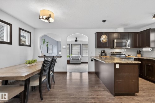 Kitchen featuring dark wood-finish cabinetry, stainless steel appliances, a white subway tile backsplash, and a peninsula with a stone-finish countertop - 108 Hewitt Circle, Spruce Grove, AB - Indoor