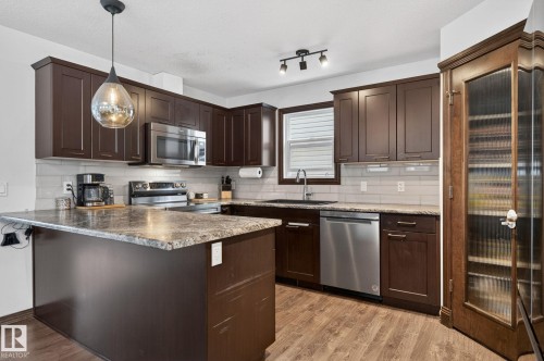 Kitchen featuring dark wood cabinetry, stainless steel appliances, a grey subway tile backsplash, and wood-finish flooring - 108 Hewitt Circle, Spruce Grove, AB - Indoor Photo Showing Kitchen With Upgraded Kitchen
