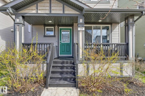 Inviting covered front porch with dark railings and steps, complemented by a vibrant green entry door with decorative glass - 108 Hewitt Circle, Spruce Grove, AB - Outdoor
