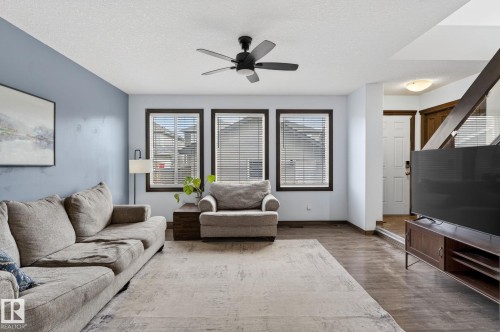 Living area featuring wood-finish flooring, a ceiling fan with integrated lighting, and three framed windows - 108 Hewitt Circle, Spruce Grove, AB - Indoor Photo Showing Living Room