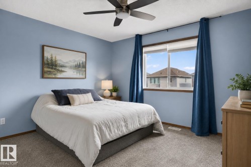 Bedroom featuring light blue walls, a ceiling fan with integrated lighting, a large window with white framing, and neutral tone carpeting - 108 Hewitt Circle, Spruce Grove, AB - Indoor Photo Showing Bedroom