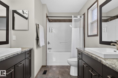 Bathroom featuring dual dark wood vanities with light stone-look countertops, rectangular undermount sinks, and brushed nickel fixtures - 108 Hewitt Circle, Spruce Grove, AB - Indoor Photo Showing Bathroom