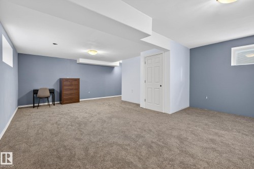 Spacious room featuring neutral carpet flooring, blue-painted walls, white trim, and a white paneled door - 108 Hewitt Circle, Spruce Grove, AB - Indoor