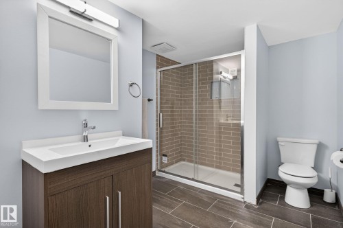 Bathroom featuring a vanity with a white countertop and wood-finish cabinetry, a framed mirror, a glass-enclosed shower with subway tile surround, and tile flooring - 108 Hewitt Circle, Spruce Grove, AB - Indoor Photo Showing Bathroom