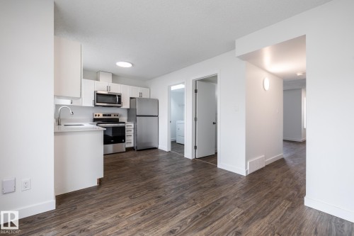 Open-concept kitchen featuring white cabinetry, stainless steel appliances, and light-toned countertops - #136, 180 Bridgeport Bv, Leduc, AB - Indoor Photo Showing Kitchen