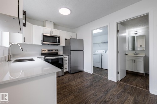 Kitchen featuring stainless steel appliances, white cabinetry with dark hardware, a single-basin sink with a gooseneck faucet, and light-colored countertops - #136, 180 Bridgeport Bv, Leduc, AB - Indoor Photo Showing Kitchen